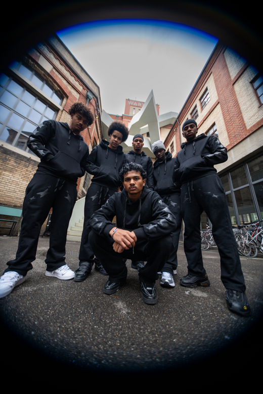 Group of people in black outfits standing in an urban setting with a fisheye lens effect.
